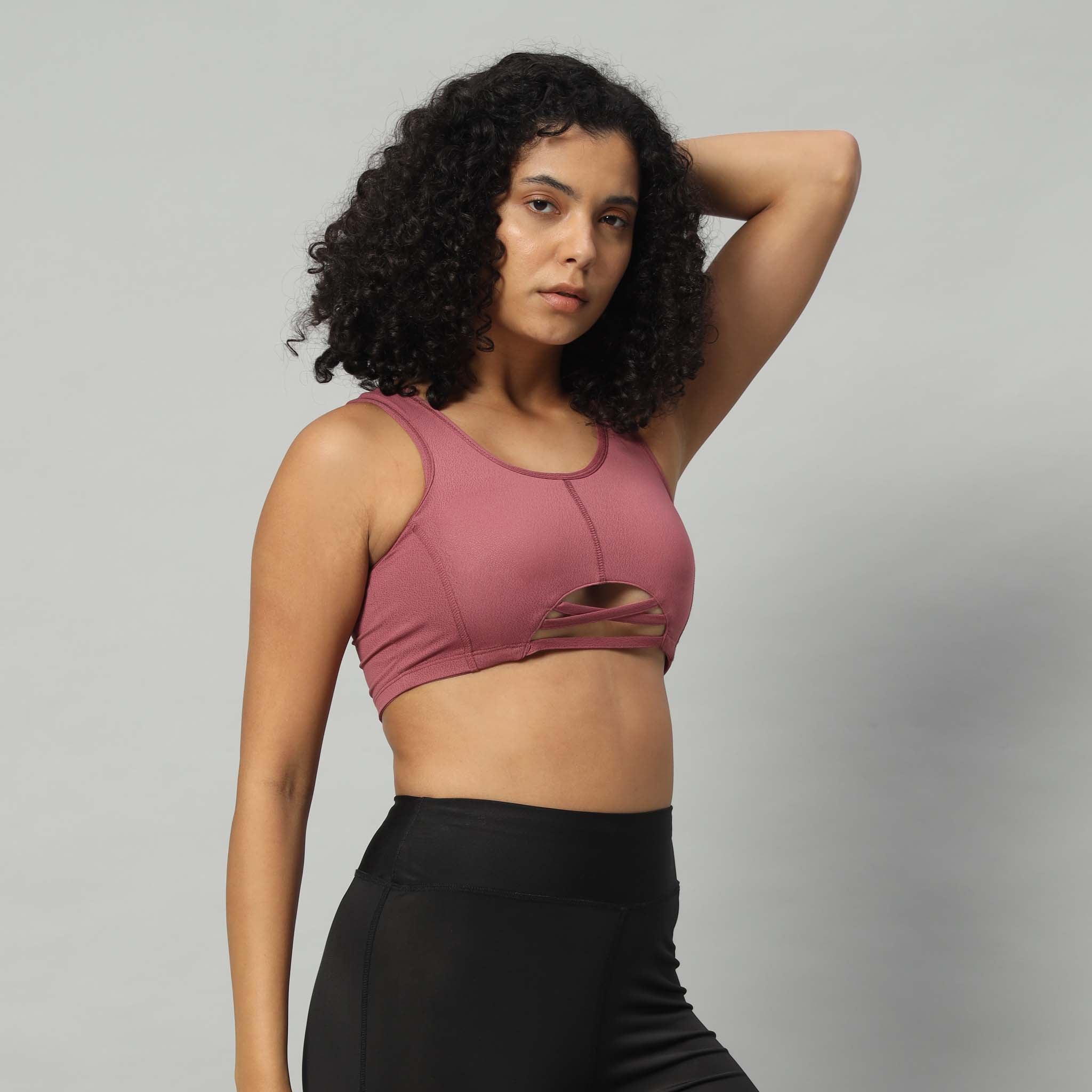 A woman wearing a pink dry fit sports bra top with a crisscross front design and a removable pad, paired with black leggings.
