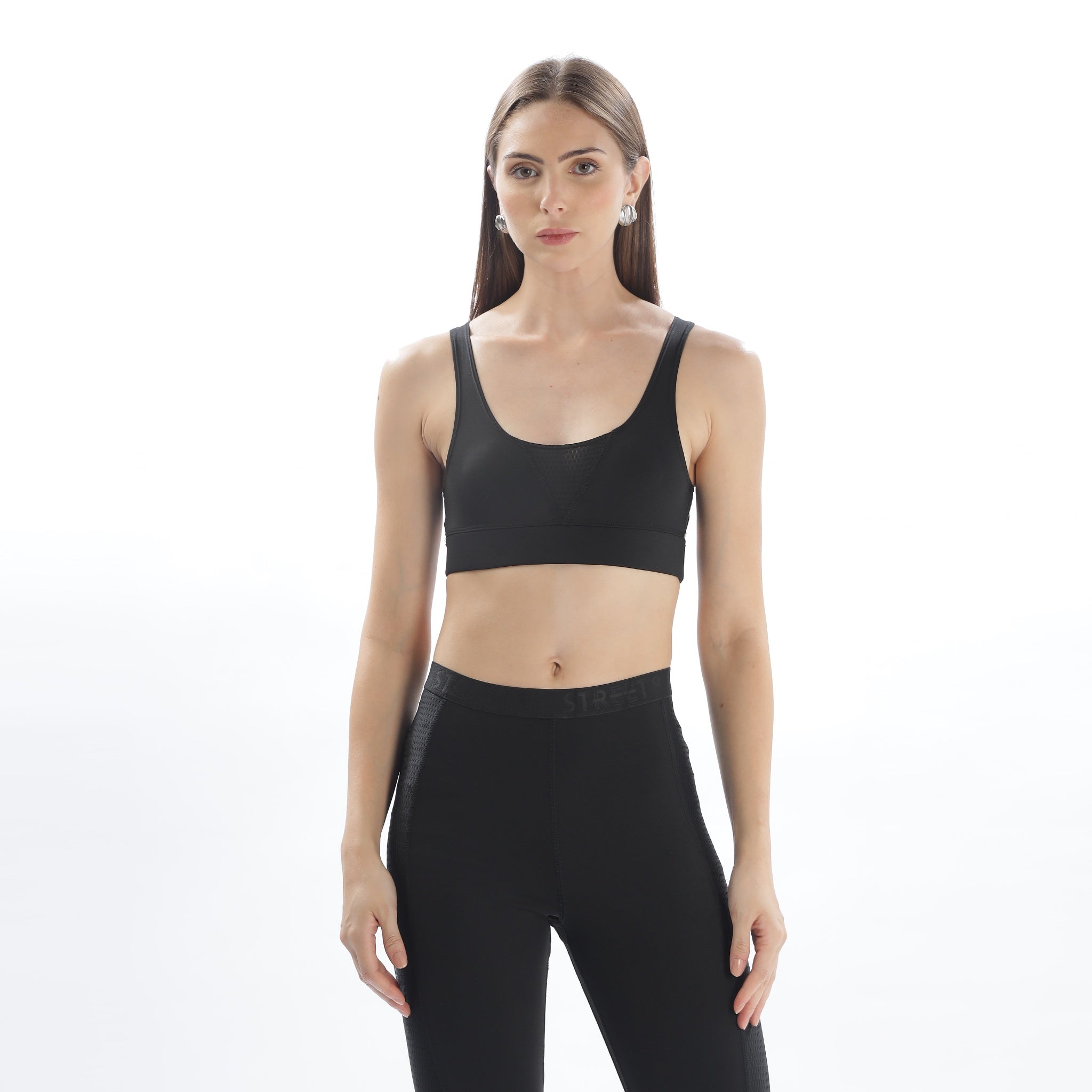 A woman wearing a black sports bra top with an adjustable strap and racerback design, paired with black activewear pants.