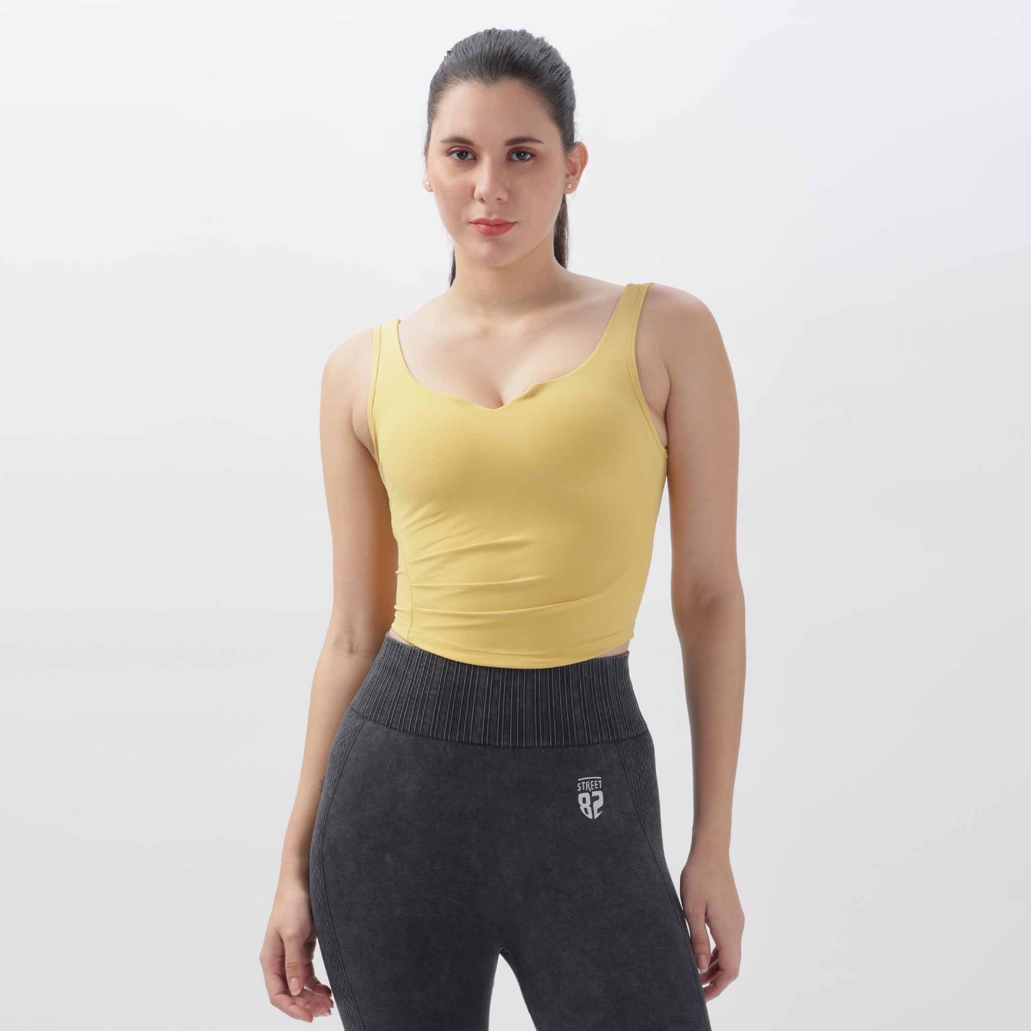 A woman wearing a yellow high support open back gym crop top and black pants.