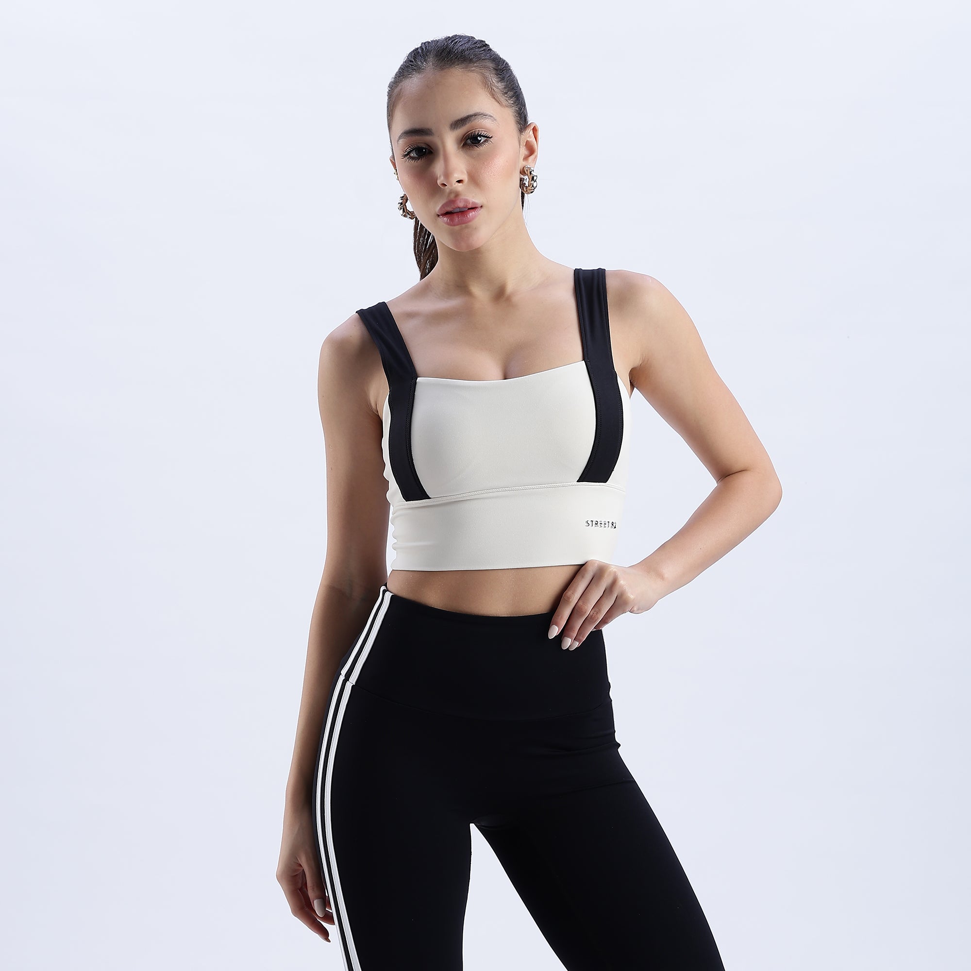 front Angle image of Woman wearing a white Evoke Sports Bra with black straps and black leggings