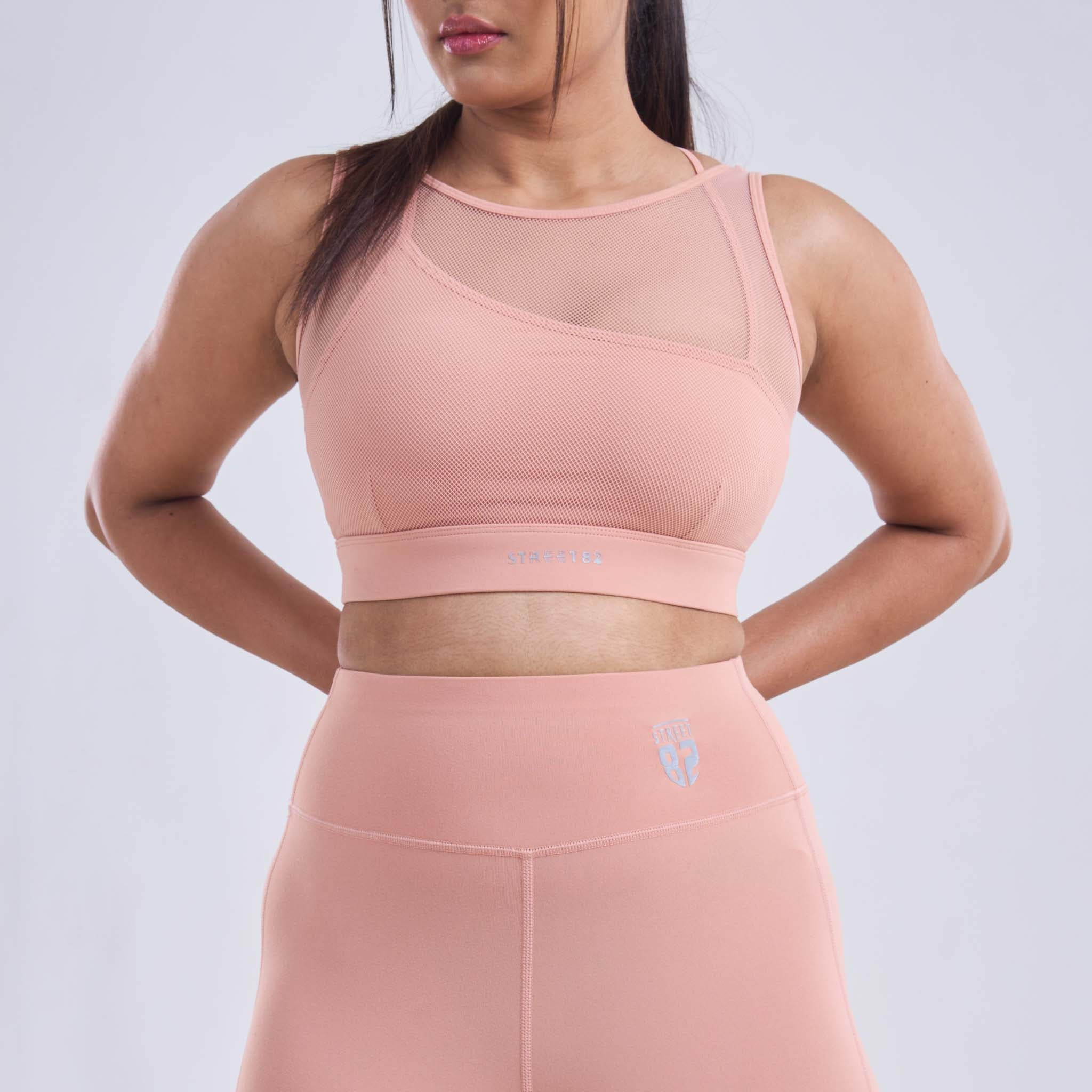 A woman wearing a pink sports bra with one shoulder design and mesh coverage on the back. The STREET82 brand logo is visible on the chest.