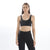 A woman wearing a black sports bra top with an adjustable strap and racerback design, paired with black activewear pants.